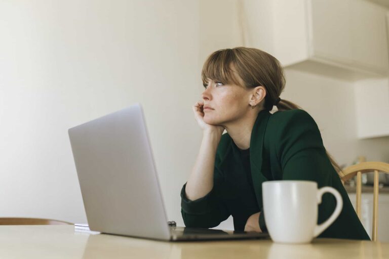 A woman experiencing a slip while sitting at a table with a laptop and a cup of coffee.