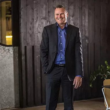 A man in a business suit standing in front of a wooden table representing Brisbane lawyers.