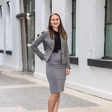 A lawyer in a grey suit standing in front of a building in Brisbane.