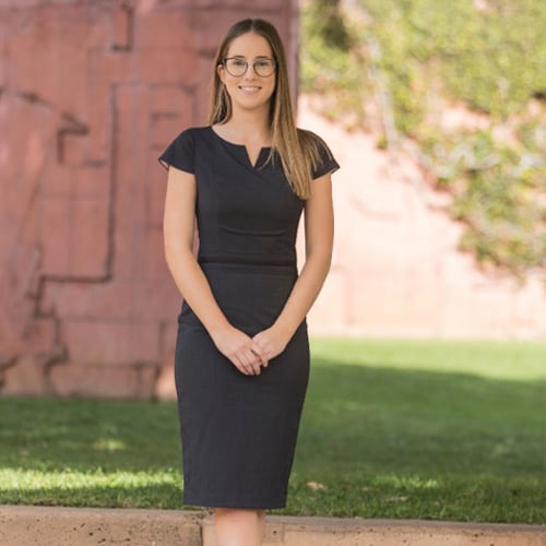 A woman named Samantha in a black dress standing in front of a brick wall.