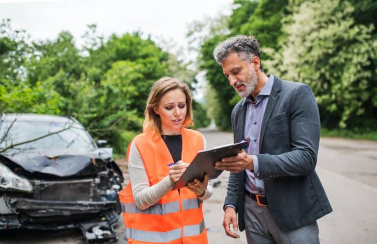 A man and woman standing next to a damaged car.