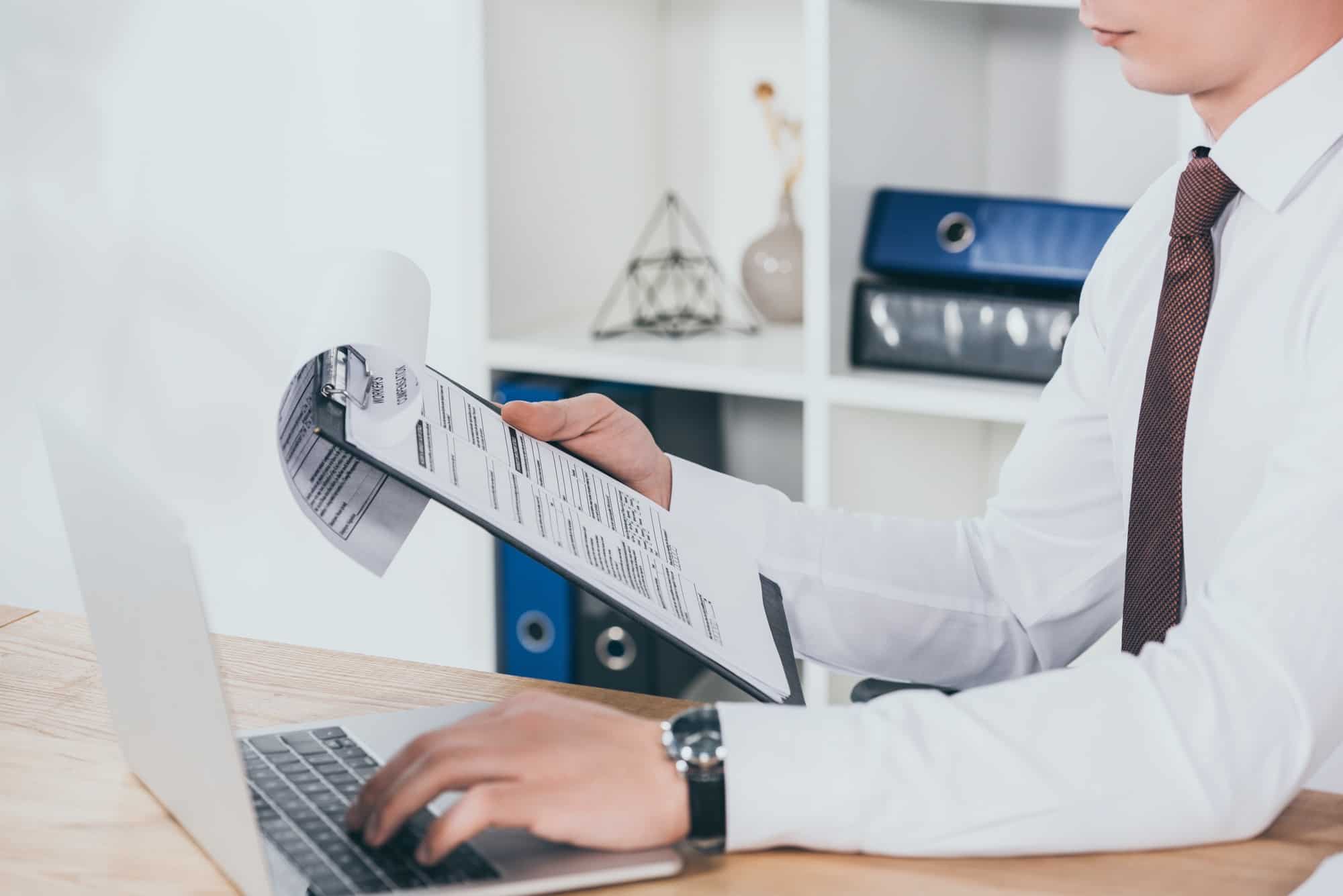 A man working on a laptop with a clipboard in front of him.