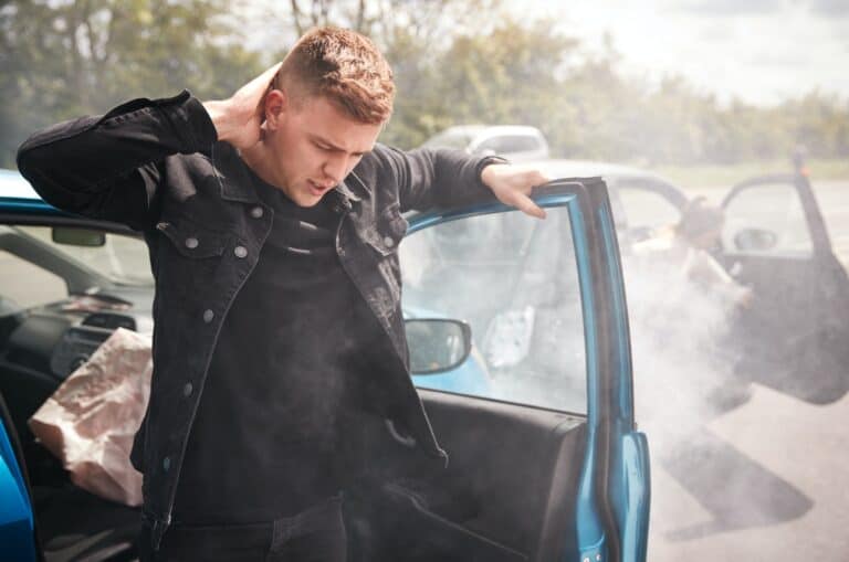 A man is standing next to a blue car with smoke coming out of it.
