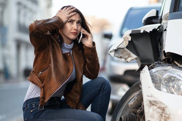 A woman talking on the phone while sitting next to a wrecked car.