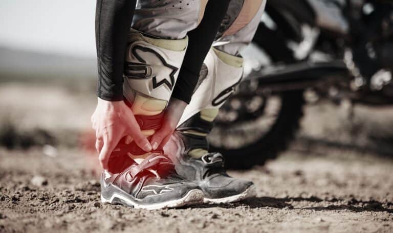 A person tying their shoes on a dirt road.