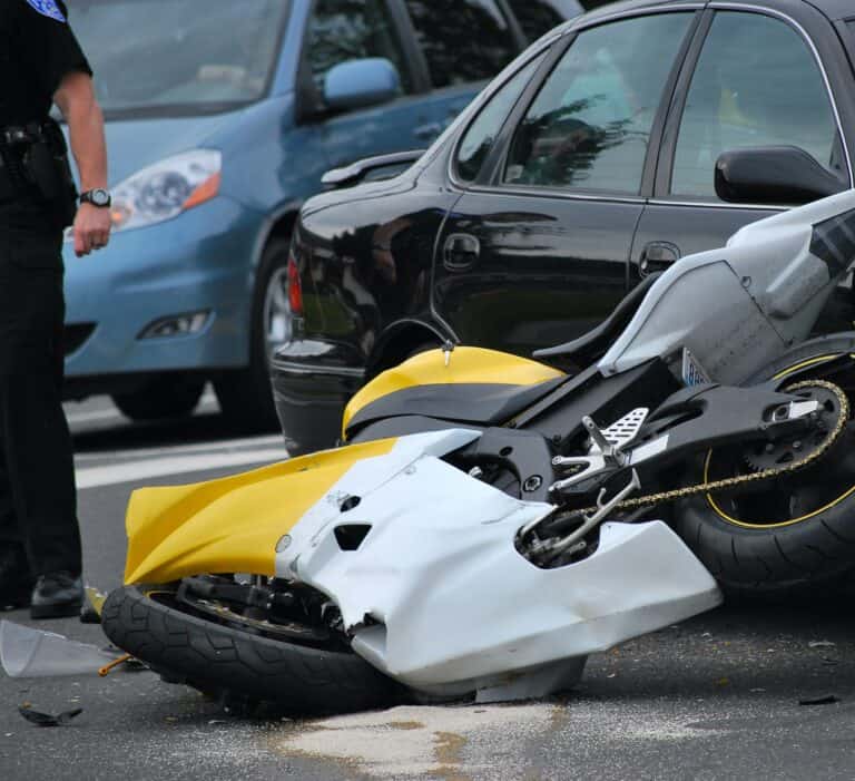 A police officer is standing next to a motorcycle that has been involved in an accident.